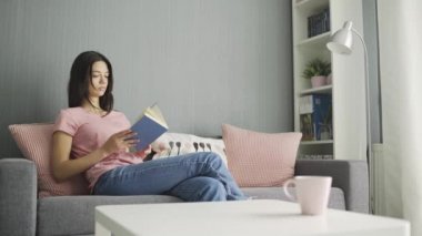 Kitap okuyan ve evdeki kanepede yatan bir kadın.