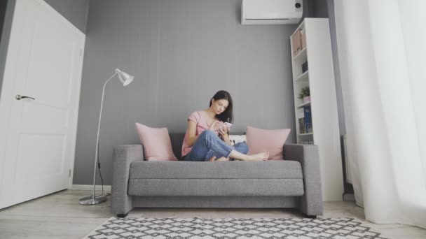 Jovem mulher bonita usando telefone enquanto sentado em um sofá em casa . — Vídeo de Stock