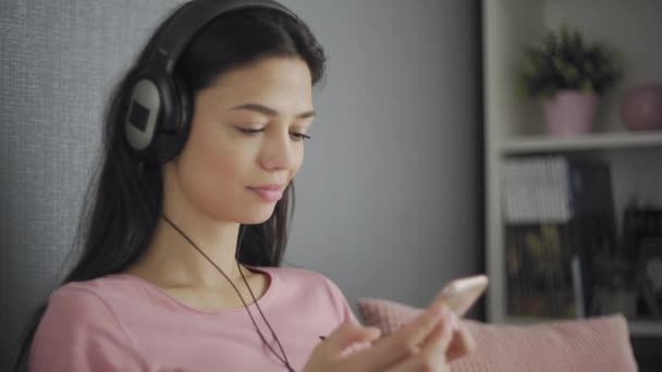 Счастливый подросток слушает музыку, расслабляясь на диване дома — стоковое видео