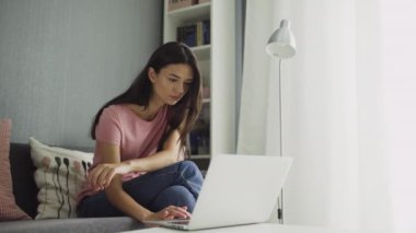 Dizüstü bilgisayarla çalışan seksi kadın evde rahat oturuyor.