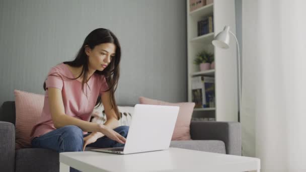 Donna guarda le notizie usando guardando il computer portatile di casa seduto sul divano. Giovane casalinga controllando i social network schermo feed seduto sul divano in soggiorno — Video Stock