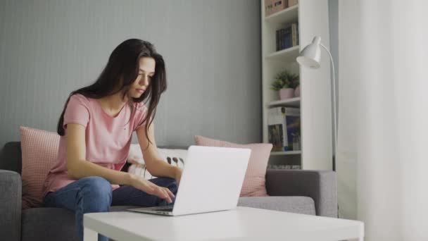 在笔记本电脑上工作的年轻女商人坐在家里的沙发上. — 图库视频影像