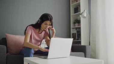Kulaklıklı genç bir kadın ekran laptopuna bakıyor ve klavyede daktilo yazıyor.