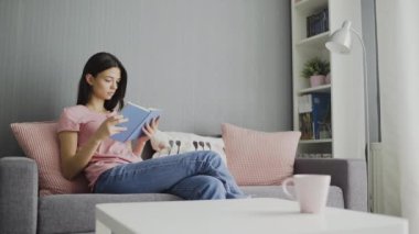 Kitap okuyan ve evdeki kanepede yatan bir kadın.