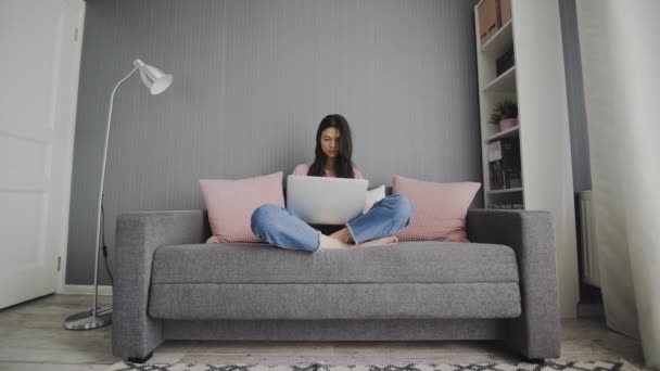 若い女性のフリーランスは、ラップトップ上でホームタイプの電子メールからフリーランスで作業します,ソファに座って自宅でオンライン学習のためのコンピュータを使用して焦点を当てた女の子,距離インターネットの仕事で忙しい女性のユーザー — ストック動画
