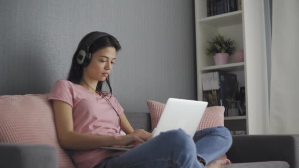 Серйозна молода жінка-фрілансер, яка працює над фрілансером з дому, друкуючи електронну пошту на ноутбуці, зосереджена дівчина використовує комп'ютер для навчання онлайн вдома, сидячи на дивані — стокове відео