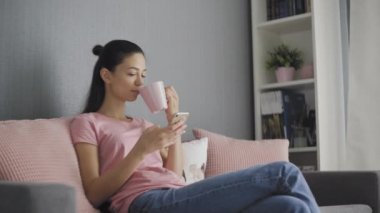 Akıllı telefonu dokunmatik ekranla kullanan ve sabahları kahve içen genç bir kadın.