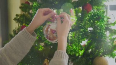 Kadınların elleri renkli toplarla Noel ağacını süslüyor.