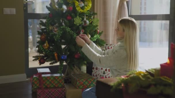 Chica bonita en suéter decora el árbol de Navidad por bolas amarillas. Interior hermoso de Navidad . — Vídeos de Stock