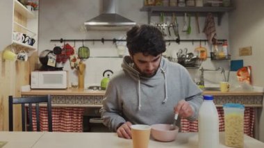 Genç bir adam mutfakta kahvaltı yapıyor. İnsan mısır gevreği yer.