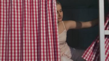 Ortak pansiyondaki genç kadın perdeleri açar ve yataktan kalkar.