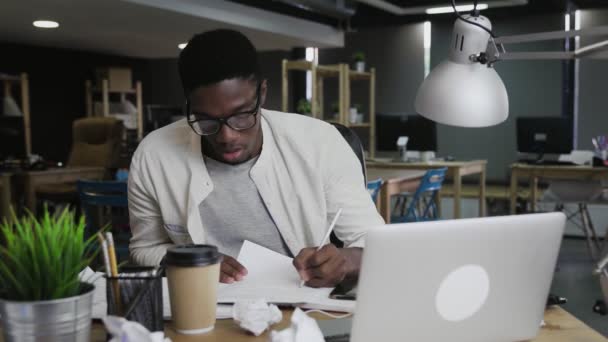 Trött afroamerikansk affärsman arbetar vid skrivbordet kasta ut papper — Stockvideo