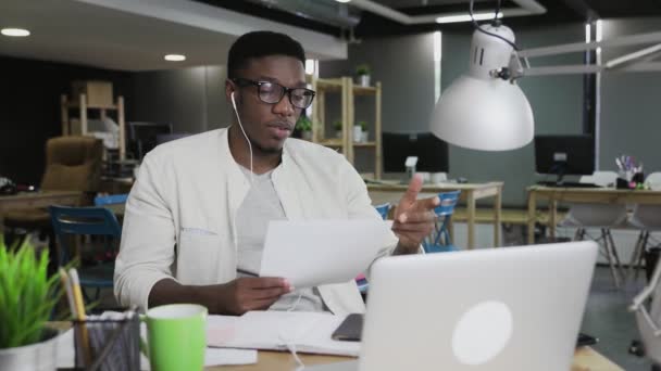 Afrikansk man med hörlurar har en videokonferens konversation i moderna kontor — Stockvideo