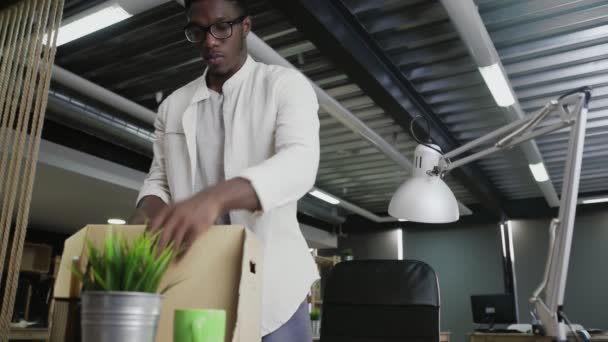 Den afrikanske mannen flyttar till ett nytt kontor. Han packar personliga tillhörigheter till kartongen. — Stockvideo