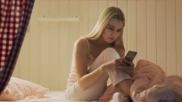 Close-up van jonge aantrekkelijke vrouw zitten op het bed in het hostel kamer, klaar met behulp van smartphone en gaan slapen — Stockvideo