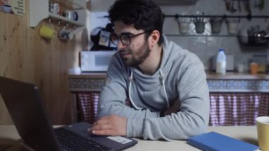Mutlu genç işadamı geceleri evdeki mutfakta dizüstü bilgisayarla çalışıyor.