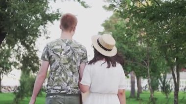 Genç çift ellerinde alışveriş torbalarıyla yaz parkında yürüyor.
