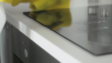 Mutfakta, sarı lastik eldivenli bir kadın tarafından yağlı temizleme spreyi ve sarı paçavrayla temizleniyor..