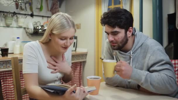 Pareja joven bebiendo té y discutiendo un libro en una cocina — Vídeos de Stock