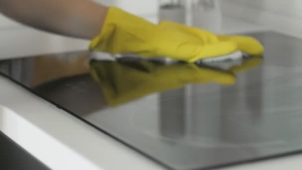 Cleaning cooktop cooking panel in kitchen with fat remover spray and white rag by a woman in yellow rubber gloves. — Stock Video