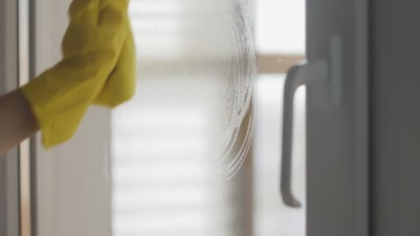 Huisvrouw in gele handschoenen wassen ramen met gele doek en wasmiddel. — Stockvideo