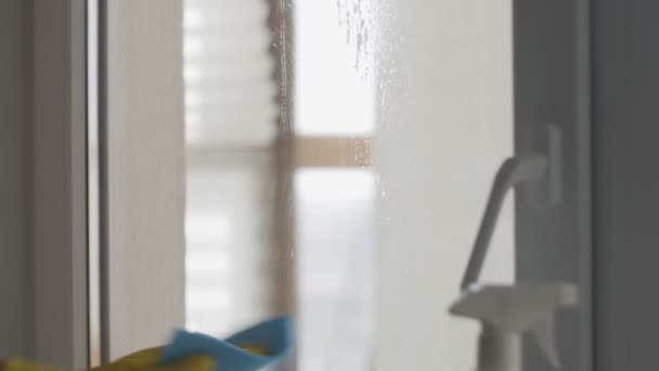 Hausfrau in gelben Handschuhen wäscht Fenster mit blauem Lappen und Waschmittel. — Stockvideo