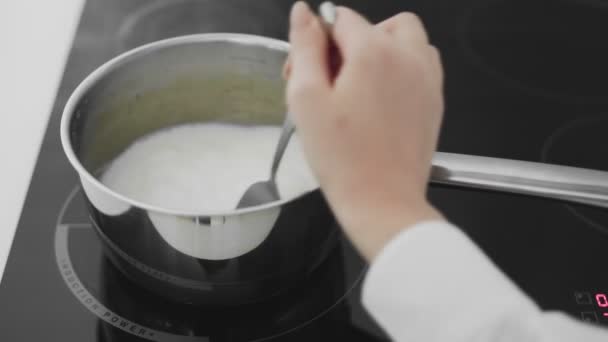 The cows milk boils in a saucepan. Woman stirs milk in saucepan — Stock Video