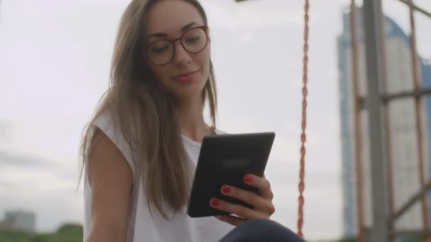 Beautiful woman in glasses reading ebook in park — Stock Video