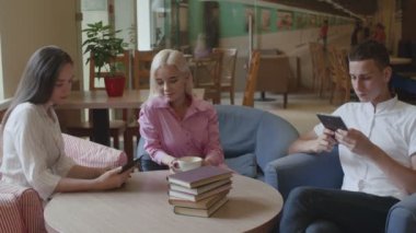 İki kız ve bir adam kafede kahve içip kitap okuyorlar.