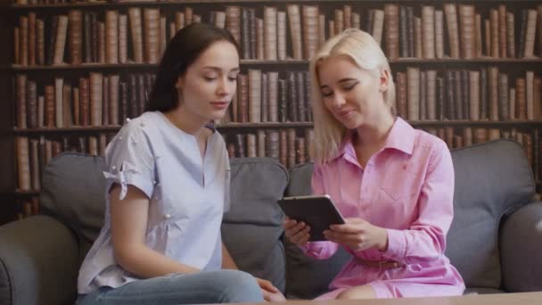 Dwie szczęśliwe kobiety czytają ebook w kawiarni. — Wideo stockowe