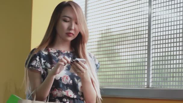 Joven mujer asiática con bolsas de compras usando el teléfono inteligente . — Vídeo de stock