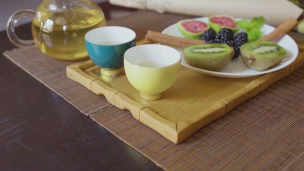 Чайник с зеленым чаем, две чашки и фрукты — стоковое видео