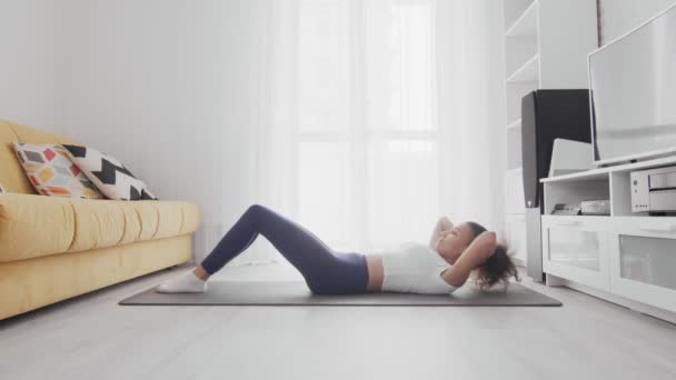 En ung, sportslig, amerikansk kvinne som trener mageknip hjemme på yogamatte. – stockvideo