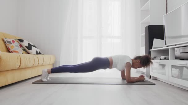 Genç Afro-Amerikan kadın evde antrenman yaparken yoga minderinde statik kalas yapıyor. — Stok video