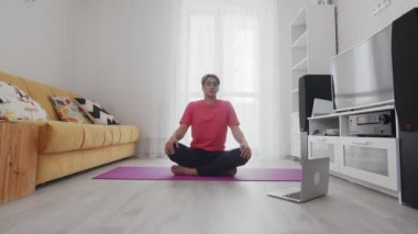 Makyajlı genç travesti homoseksüel adam egzersizden önce ısınmak için döner ve evdeki dizüstü bilgisayara bakar.