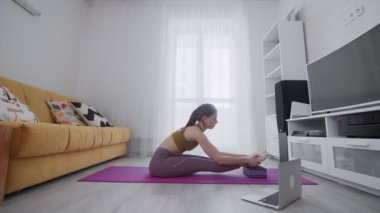 Genç ve güzel bir kadın evde menekşe paspası üzerinde esneme egzersizleri yapıyor.