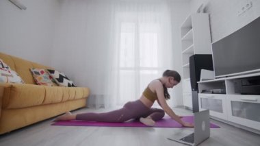 Genç ve güzel bir kadın evdeki menekşe paspasın üzerinde bacak egzersizi yapıyor.