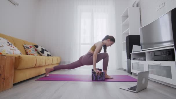 Joven hermosa mujer está practicando piernas estiradas en estera violeta, ella usando dos ladrillos para apoyar — Vídeos de Stock