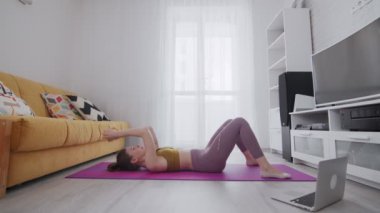 Dövmeli genç bir kadın minder üzerinde karın kasları egzersizi yapıyor.