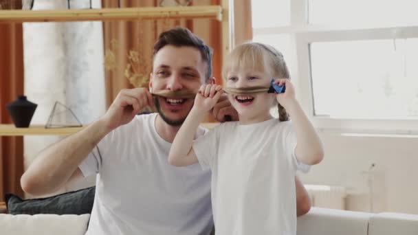 Lustiger Vater und seine Tochter machen Schnurrbart und posieren. Vatertagskonzept — Stockvideo