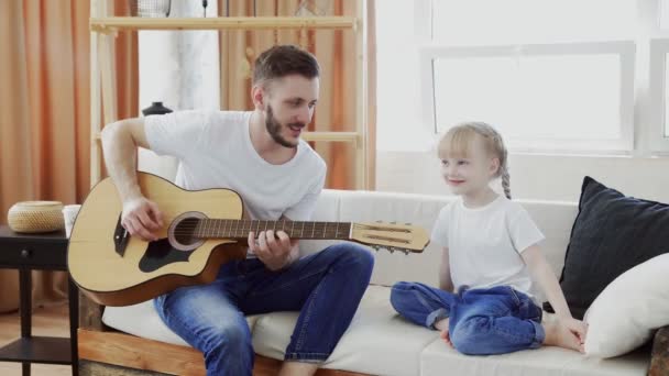 Młody ojciec siedzi z Dauhterem i gra na gitarze. Koncepcja dnia ojców — Wideo stockowe