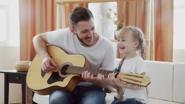 Giovane padre insegna figlia a suonare la chitarra a casa — Video Stock
