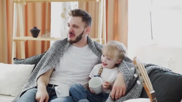 El joven padre y su hija se sientan en un sofá cubierto con manta y charlas — Vídeos de Stock