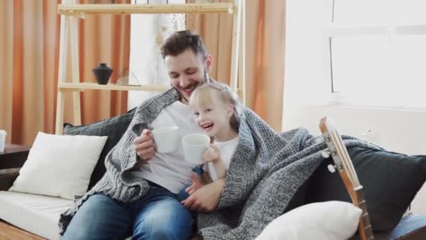 El joven padre y su hija se sientan en una manta cubierta de sofá con grandes vasos blancos y charlas — Vídeo de stock