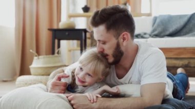 Mutlu baba ve kızı yerde yatıyor. Sakallı baba küçük tatlı kızını öpüyor.