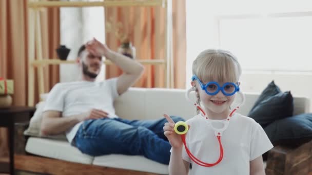 Little funny kid girl dressed in medical uniform playing as doctor with father at home — Stock Video