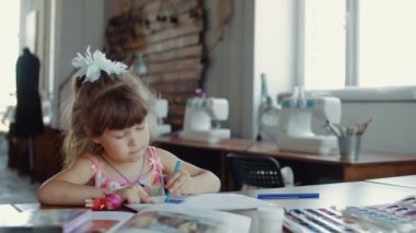 Masada renkli kalemlerle çizim yapan bir kız resmi.