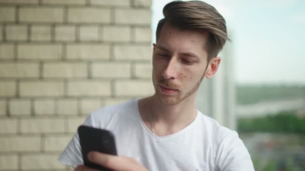 Junger Mann im weißen T-Shirt surft mit seinem Smartphone im Internet — Stockvideo