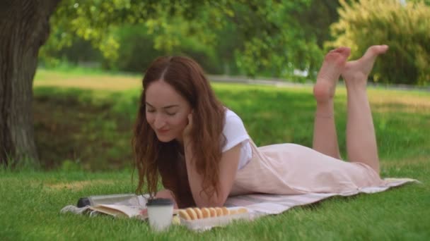 Молода жінка лежить і читає книгу в парку — стокове відео