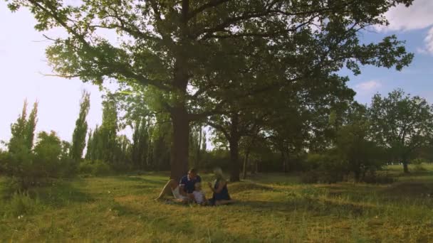 Gelukkig gezin picknicken onder de boom — Stockvideo